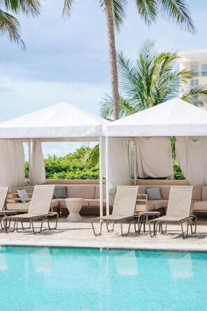 A poolside area with lounge chairs and a canopy, surrounded by palm trees. - Largest 2 bd ocean view @ the palm beach Marriott (Riviera Beach)