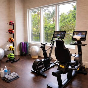 A home gym with exercise equipment, including an elliptical and a stationary bike, and a rack with various exercise balls. - Largest 2 bd ocean view @ the palm beach Marriott (Riviera Beach)