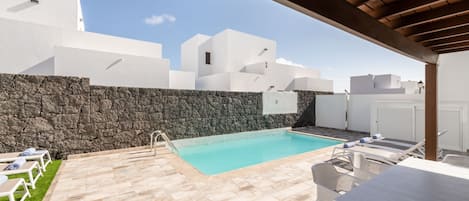 A pool area with lounge chairs, a table, and a stone wall.