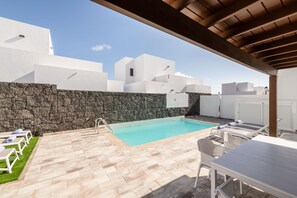 Área de piscina com espreguiçadeiras, uma mesa e um muro de pedra.