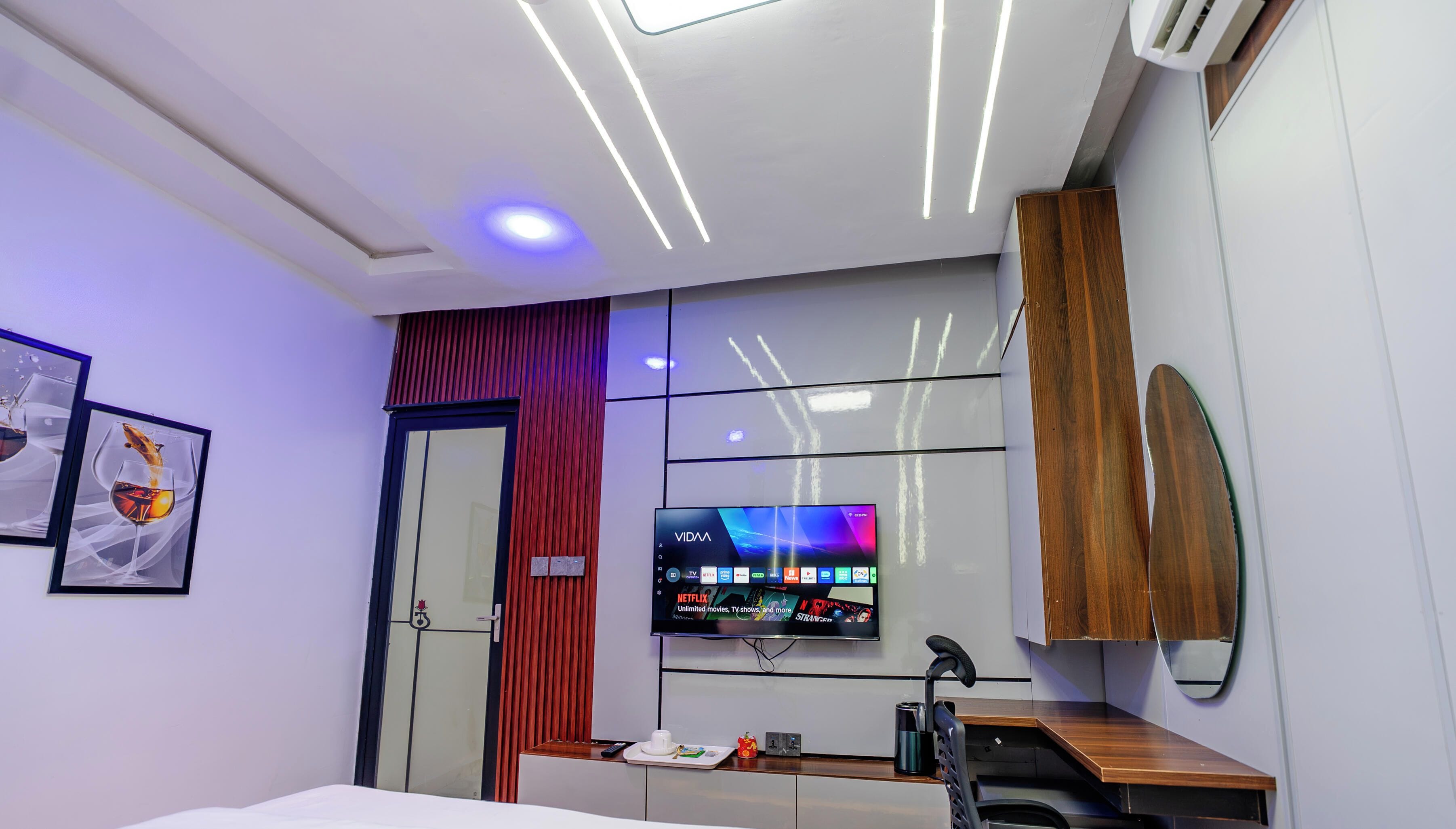 Habitación de hotel moderna con televisor de pantalla plana, un escritorio con silla, una cama y una puerta con panel de vidrio.