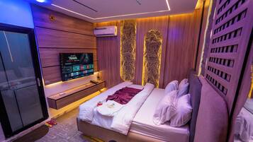 Habitación de hotel moderna con televisión de pantalla plana, cama con ropa blanca y cabecero de madera.