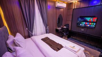 A hotel room with a bed, a desk, a chair, a television, and an air conditioning unit.