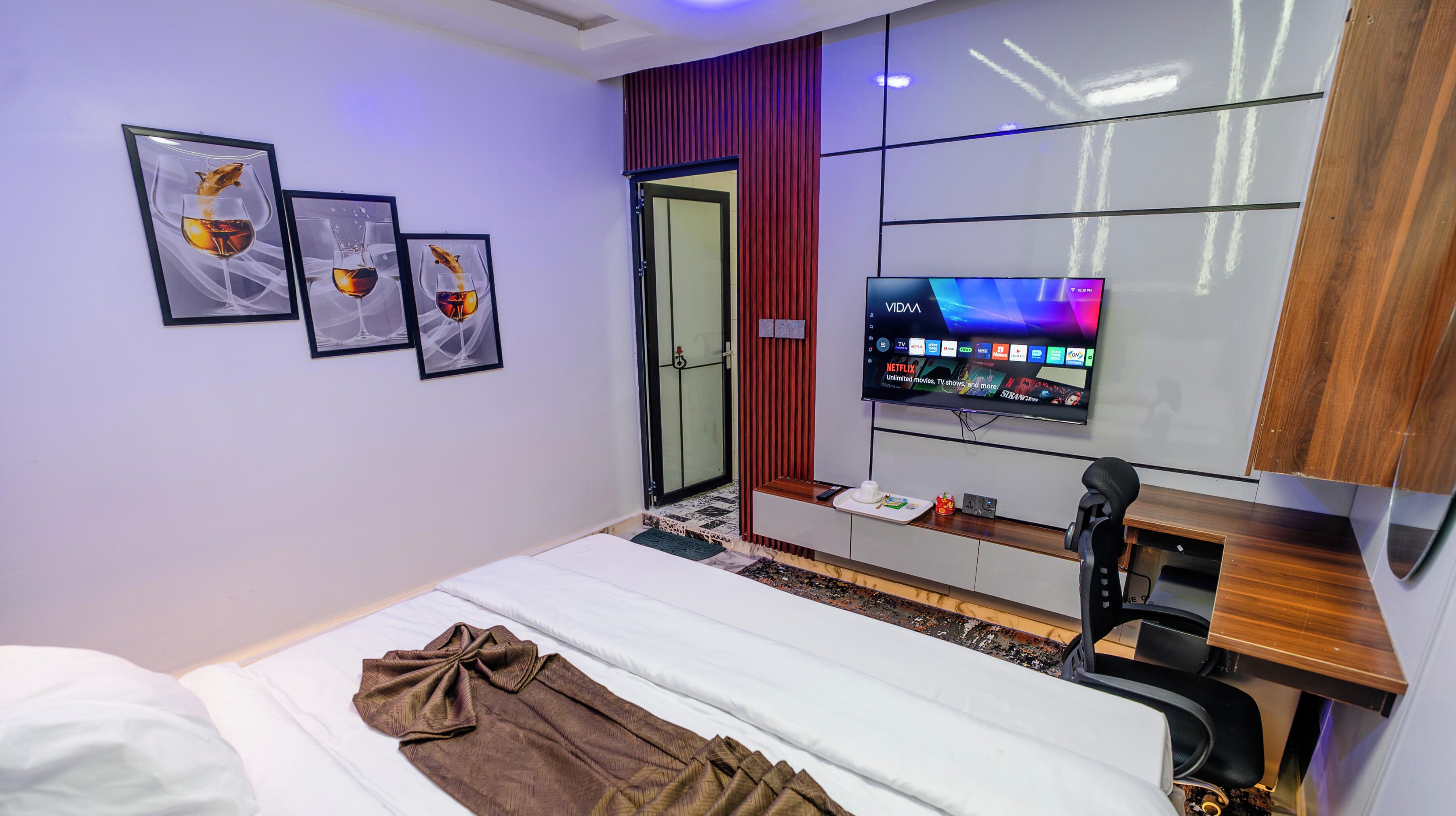 Una habitación de hotel con cama, escritorio, computadora, televisor y tres cuadros en la pared.