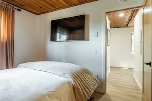 A bedroom with a bed, a television mounted on the wall, and a wooden ceiling. - Newly Remodeled Walk to Ski Condo 615 (Mammoth Lakes)