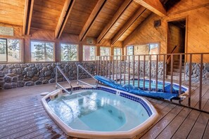 A wooden interior with a hot tub, stone walls, and a view of trees through large windows. - Newly Remodeled Walk to Ski Condo 615 (Mammoth Lakes)