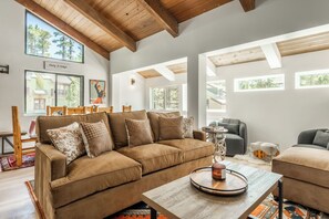 A spacious living room with a large brown sofa, a wooden coffee table, and multiple windows providing natural light. - Newly Remodeled Walk to Ski Condo 615 (Mammoth Lakes)