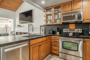 A modern kitchen with stainless steel appliances, wooden cabinets, and a built-in dishwasher. - Newly Remodeled Walk to Ski Condo 615 (Mammoth Lakes)
