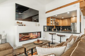 A modern kitchen with wooden cabinets, a stainless steel refrigerator, and a bar area with stools. - Newly Remodeled Walk to Ski Condo 615 (Mammoth Lakes)