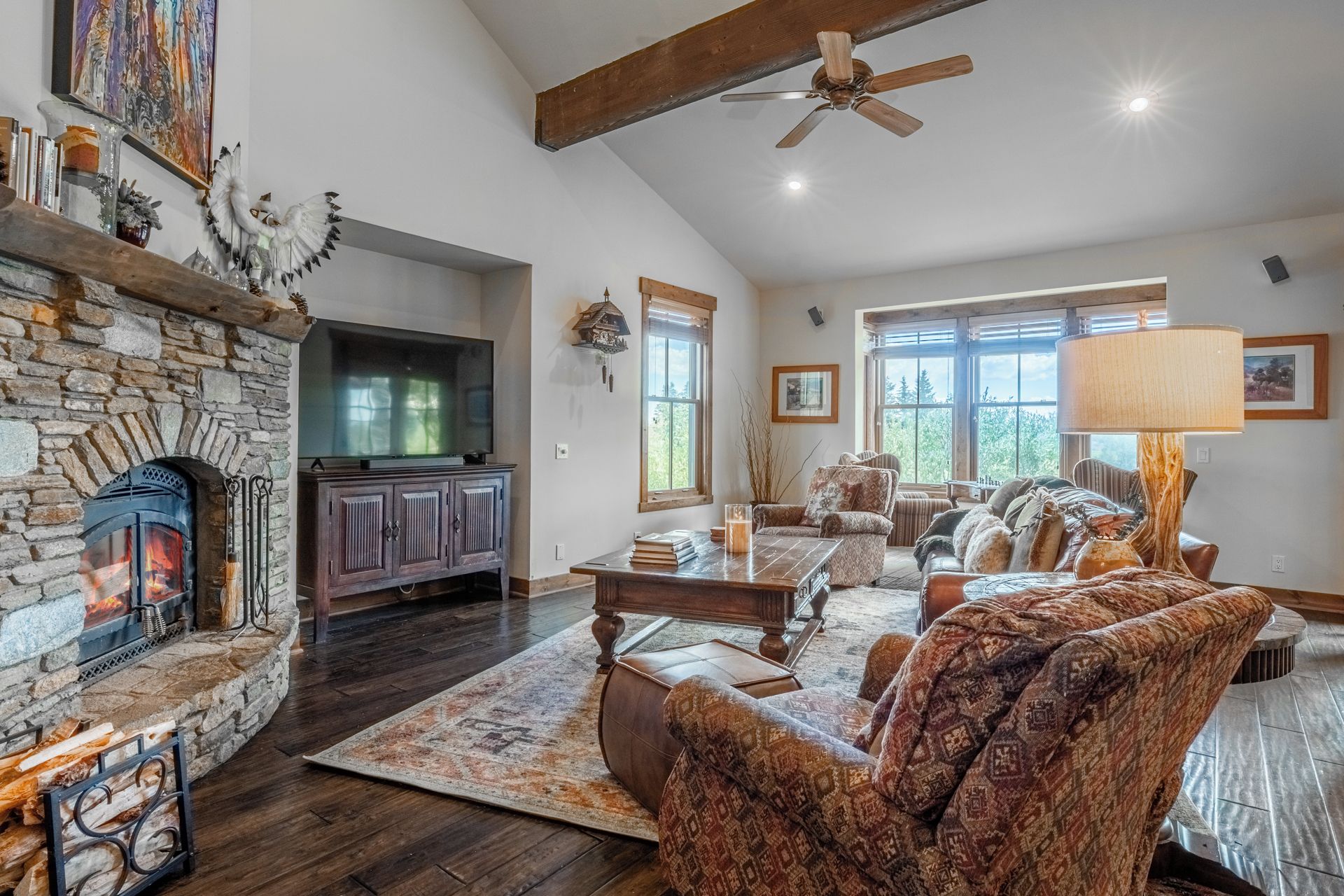 A spacious living room with a stone fireplace, a television, and a large window.