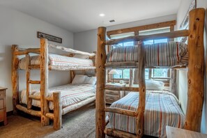 A bunk bed room with a rustic wooden design, a small table with a lamp, and a window with a view. - Lodges Condo Mountain Views 507 (Mammoth Lakes)