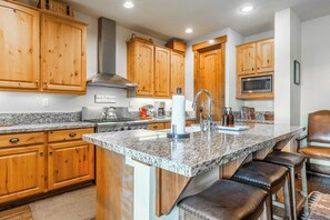 A kitchen with wooden cabinets, granite countertops, a stainless steel stove, and a microwave. - Lodges Condo Mountain Views 507 (Mammoth Lakes)