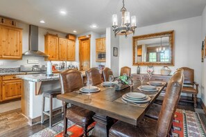 A dining area with a large wooden table, leather chairs, and a chandelier. - Lodges Condo Mountain Views 507 (Mammoth Lakes)