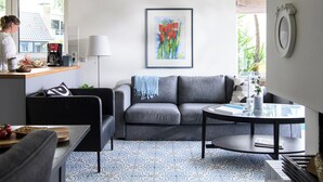 Uma sala de estar moderna com um sofá cinzento, uma mesa de centro e um chão estampado.
