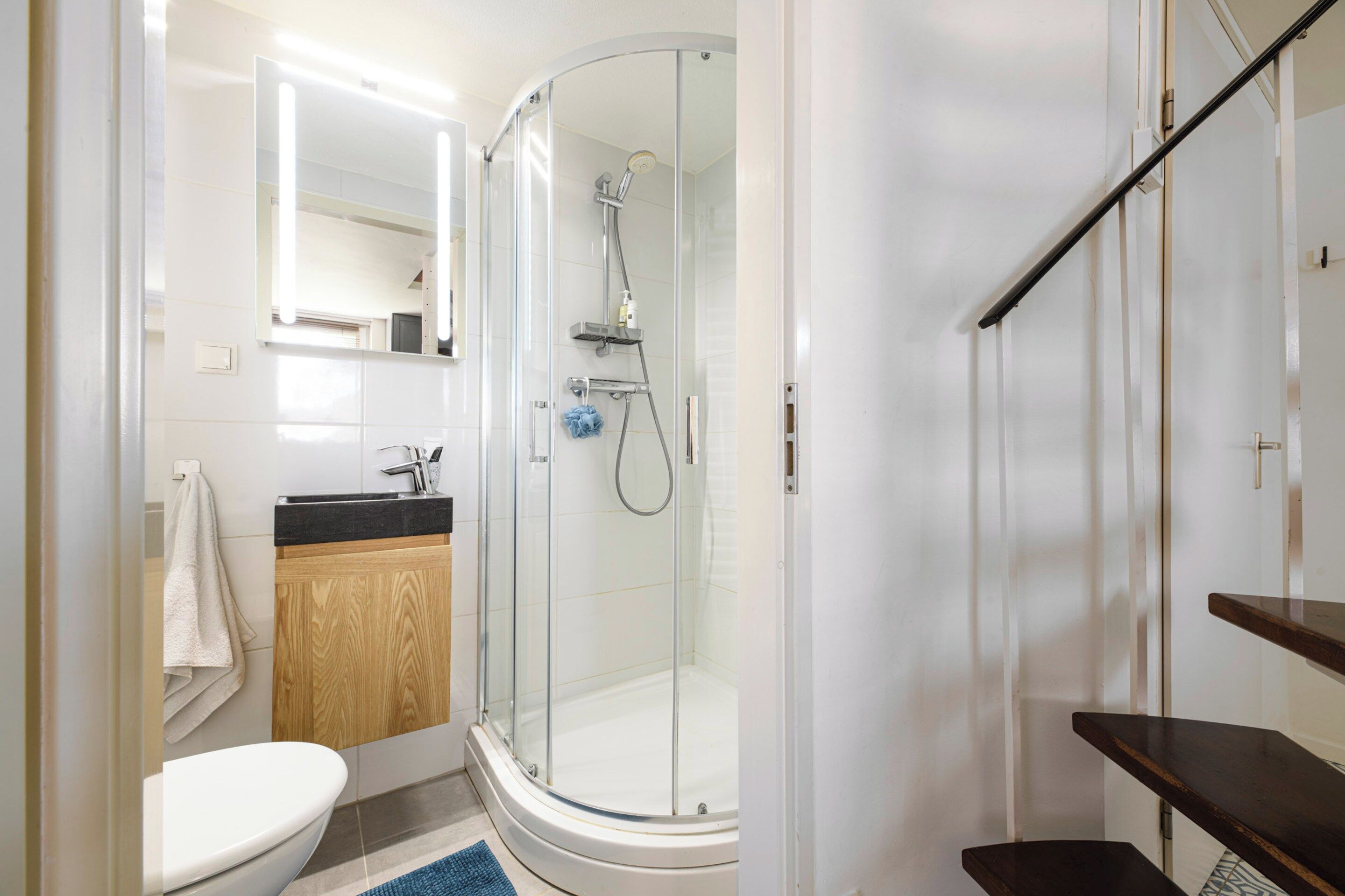 A modern bathroom with a glass-enclosed shower, a toilet, and a sink with a wooden vanity.