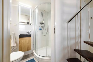 Un baño moderno con ducha envuelta en vidrio, inodoro y lavamanos con tocador de madera.