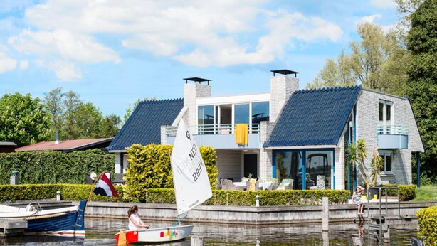 Uma casa moderna com uma varanda grande, um veleiro na água e um cais com um barco.