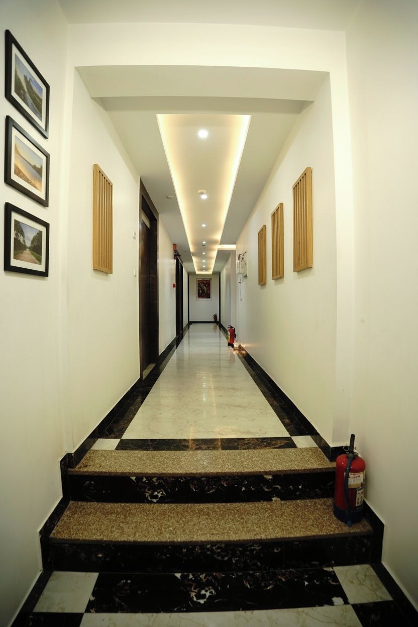 A hotel hallway with a checkered floor, framed pictures on the walls, and a fire extinguisher on the right.