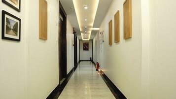 A hotel hallway with a checkered floor, framed pictures on the walls, and a fire extinguisher on the right.