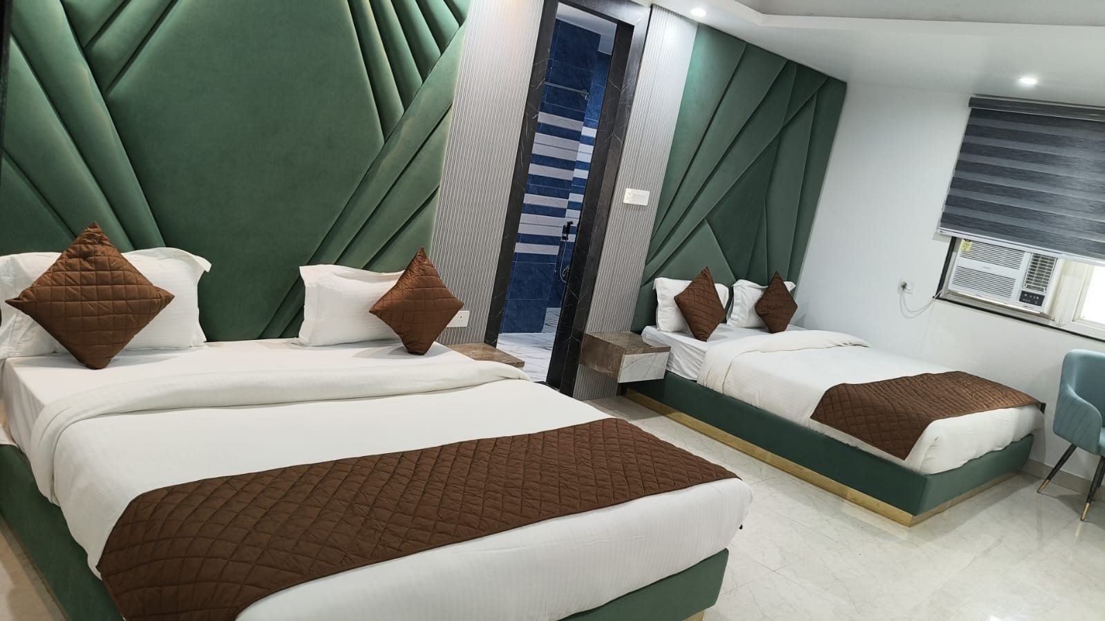Habitación de hotel con dos camas, zona de estar y ventana con unidad de aire acondicionado.