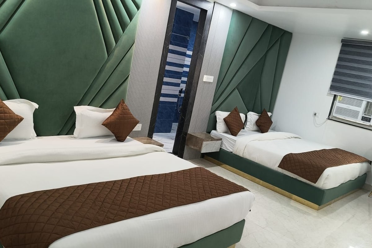 A hotel room with two beds, a seating area, and a window with an air conditioning unit.