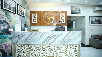 A reception desk with a marble top and decorative paneling, framed photographs on the wall, and a logo above the desk.