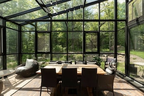 A conservatory with a dining table and chairs, surrounded by glass walls offering a view of a forest. - TOP LUXE mountain + lake VIEW | Hot Tub • Fire pit (Les Laurentides Regional County Municipality)