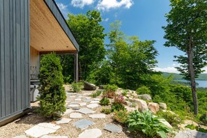 A modern building with a wooden exterior and a stone pathway leading to a scenic outdoor area with trees and a view of a lake.
