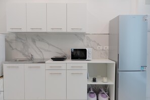 Cozinha moderna com armários brancos, micro-ondas, pia e geladeira.