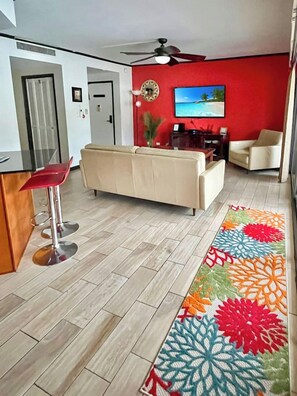A living room with a sofa, a coffee table, a TV, and a red wall. - 2 bedroom condo in the heart of downtown Kailua Kona (Kailua Kona)