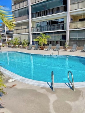 A swimming pool with a clear blue water, surrounded by lounge chairs and potted plants. - 2 bedroom condo in the heart of downtown Kailua Kona (Kailua Kona)