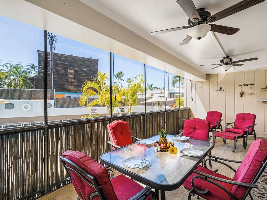 A balcony with red chairs, a table with fruit, and a view of buildings and palm trees.