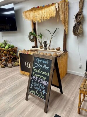 A room with a wooden table displaying coconuts and a chalkboard sign advertising free tastings. - 2 bedroom condo in the heart of downtown Kailua Kona (Kailua Kona)
