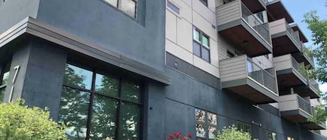 A multi-story building with balconies, large windows, and a well-maintained garden with various plants and flowers.
