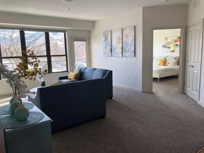 A living room with a sofa, a coffee table, and a vase with flowers. There are abstract paintings on the wall and a bed in the background. - Modern Apt a Block from St. Pat's Hospital #202 (Missoula)