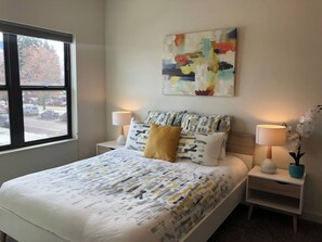 A hotel room with a bed, two bedside tables, a window, and a painting on the wall. - Modern Apt a Block from St. Pat's Hospital #202 (Missoula)