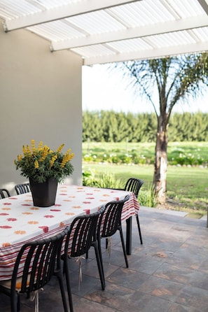 An outdoor patio with a round table, black chairs, and a potted plant with yellow flowers.