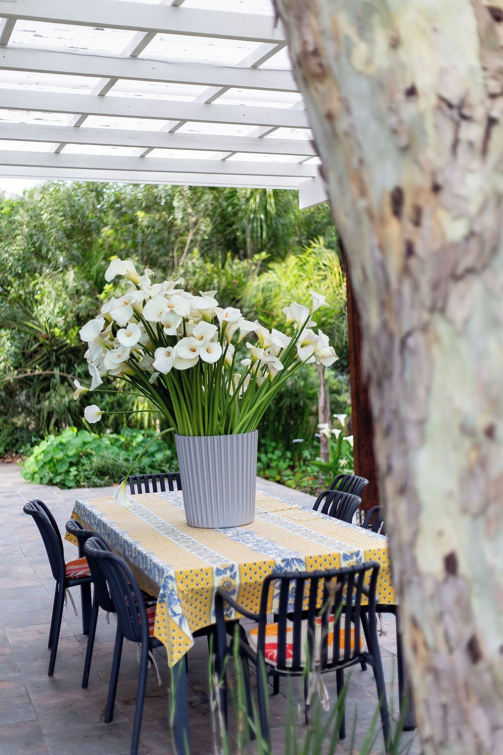 An outdoor patio with a table covered in a yellow tablecloth, surrounded by chairs.