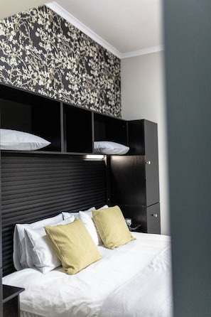 A hotel room with a bed, white bedding, a black headboard, and a wall with a floral pattern.