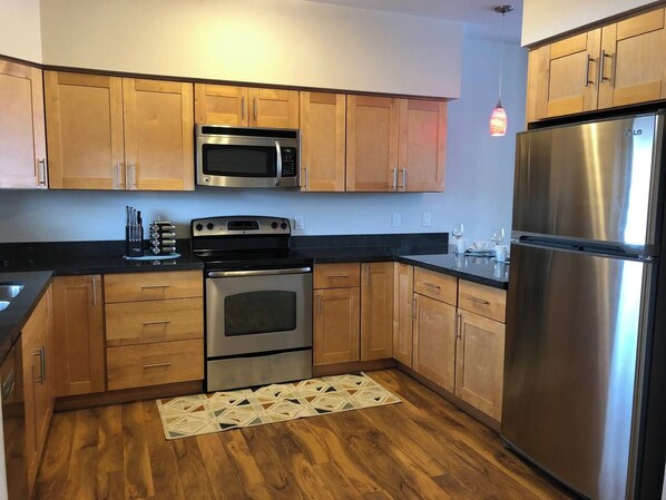 A kitchen with wooden cabinets, stainless steel appliances, and a patterned rug. - Modern Apt a Block from St. Pat's Hospital #302 (Missoula)
