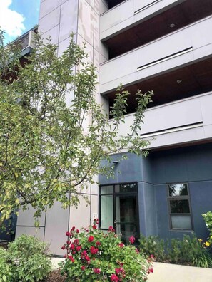 A modern building with a glass entrance, surrounded by greenery and a small garden with red flowers. - Modern Apt a Block from St. Pat's Hospital #302 (Missoula)