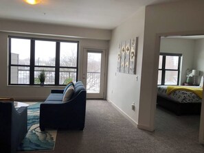 A living room with a sofa, a coffee table, and a rug. There are large windows and a door leading to another room. - Modern Apt a Block from St. Pat's Hospital #302 (Missoula)