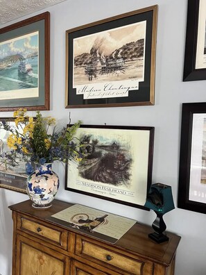A wall with framed artwork, a vase with flowers, and a wooden cabinet with a placemat. - River Living One Story 2bd/2ba - On the River - 2 Blks to Main St - VIEWS GALORE (Madison)