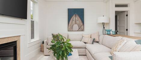 A living room with a sectional sofa, a fireplace, a television, and a painting on the wall.