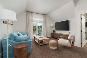 Ein modernes Wohnzimmer mit Sofa, Couchtisch und Sessel, einem Flachbildfernseher sowie einem Balkon mit Blick.