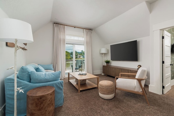 A modern living room with a sofa, coffee table, and armchair, a flat-screen TV, and a balcony with a view. - The Waterline | lakefront, dock & hot tub, pets ok (Lincoln City)