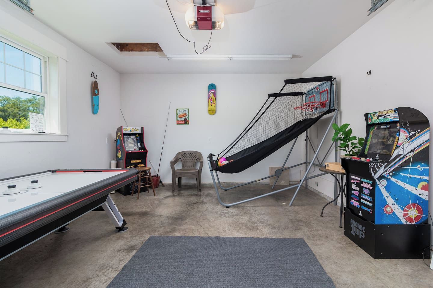 Une pièce avec une table de billard, une petite chaise, un hamac, des jeux d’arcade et une fenêtre donnant sur un beau paysage.