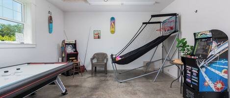 Une pièce avec une table de billard, une petite chaise, un hamac, des jeux d’arcade et une fenêtre donnant sur un beau paysage.