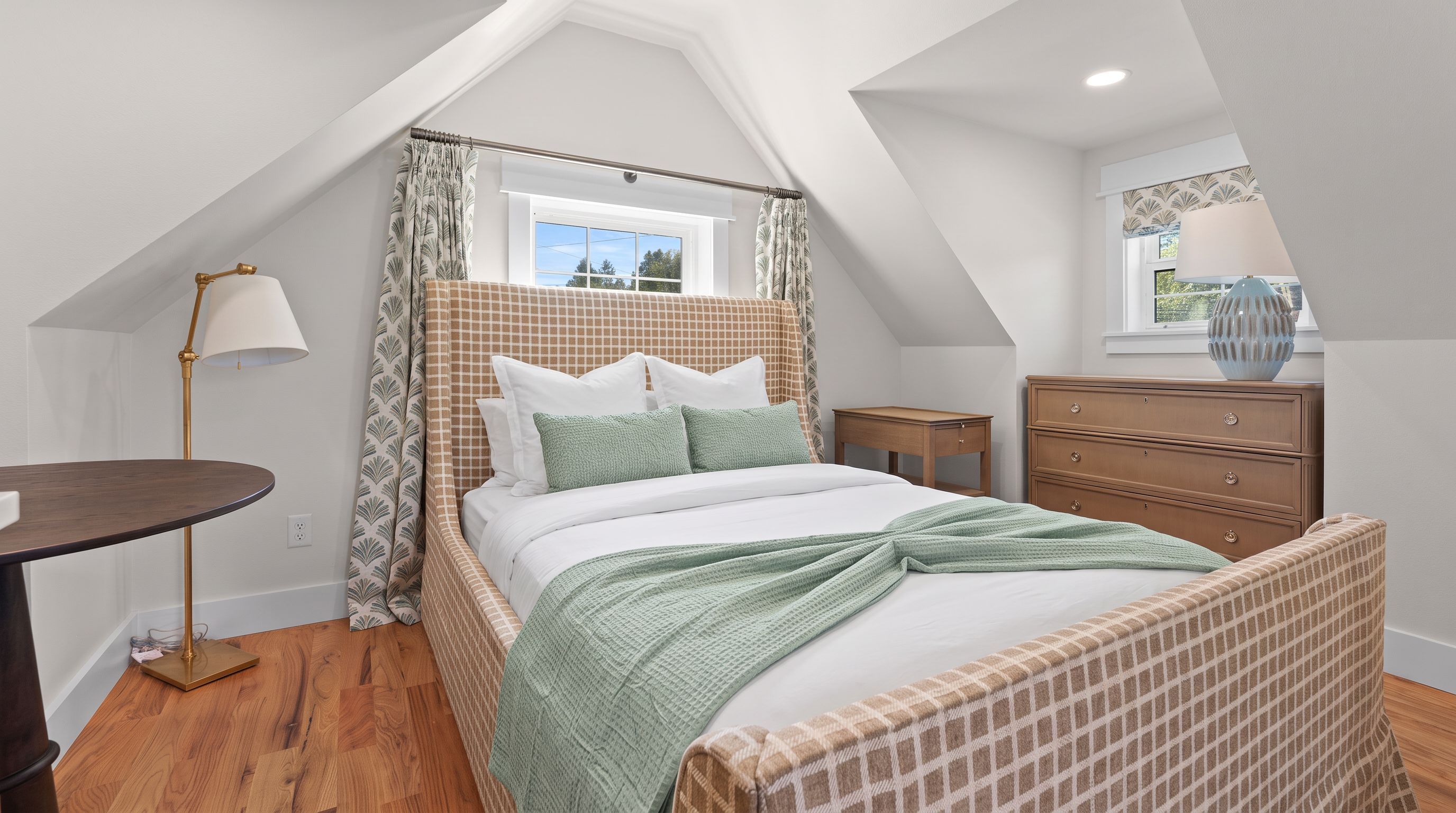 A bedroom with a bed, a dresser, a nightstand, a lamp, and a window.