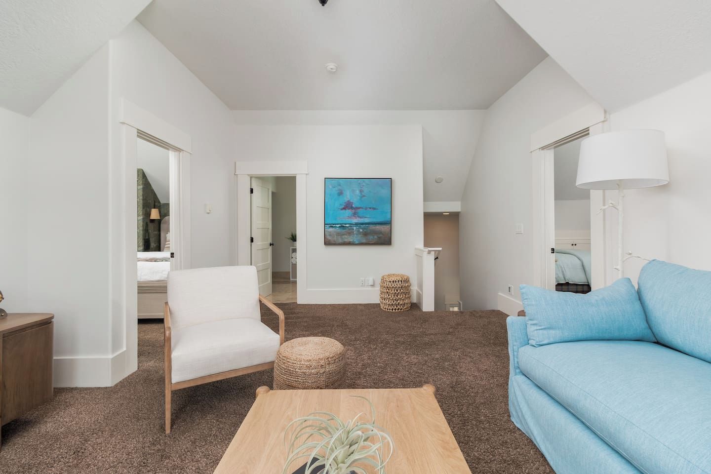 Una sala de estar moderna con un sofá blanco, un sillón blanco y una mesa de centro de madera. Hay un cuadro en la pared y una lámpara sobre una mesita auxiliar.
